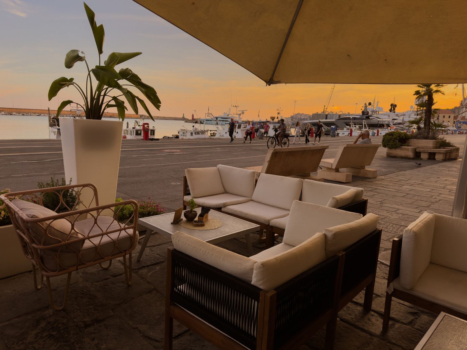 Lounge all'aperto del Chillout Zone a Imperia: divanetti bianchi sotto l'ombrellone con vista sul porto al tramonto, perfetto per l'aperitivo