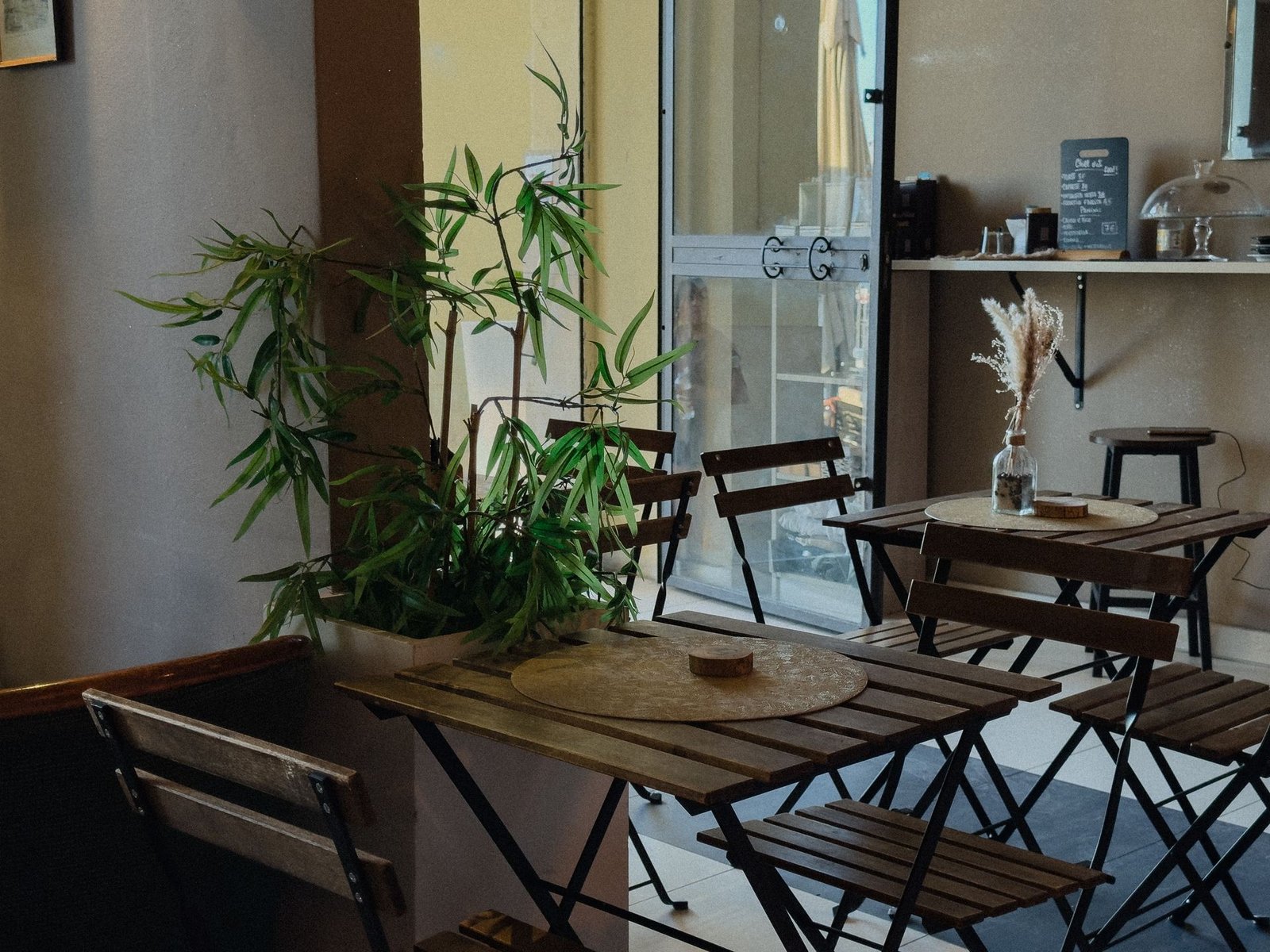 Tavolini in legno, sedie pieghevoli e piante verdi nella caffetteria del Chillout Zone a Imperia, colazioni e caffè